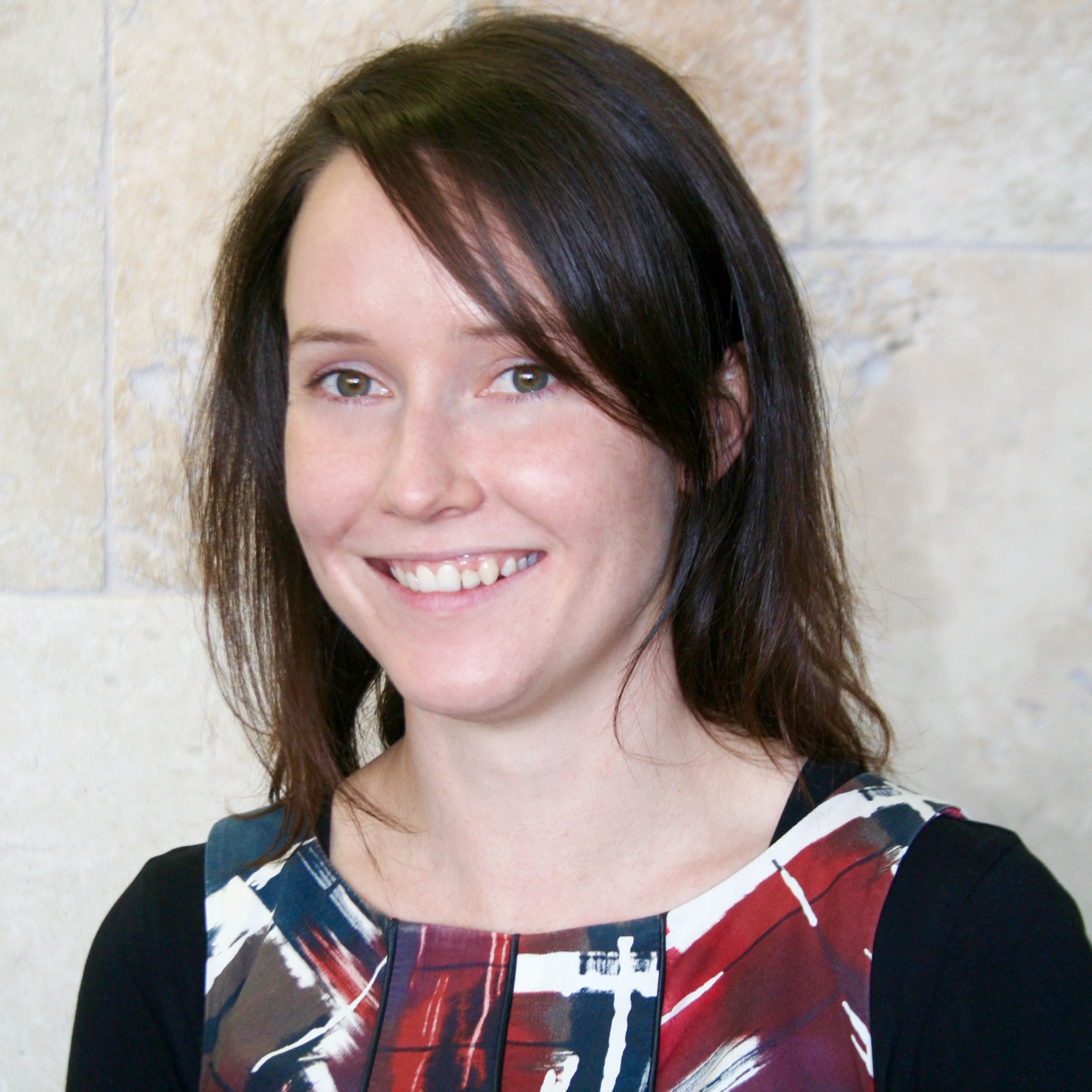 Headshot of a woman with dark hair in front of a sandstone wall.